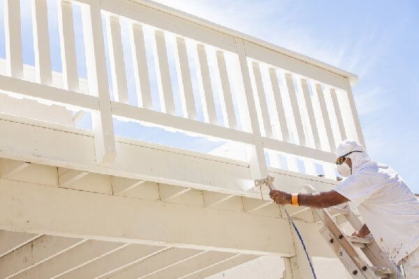 painter spraying a railing with white paint