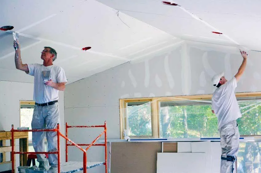 Skilled drywall finishers on scaffolding applying the final coat of mud, ensuring a flawless finish for your home renovation project. The Renovator provides expert drywall installation and finishing services in the Greater Vancouver and Fraser Valley regions.