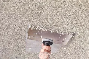 Professional technician removing popcorn ceiling texture with handheld scraper, creating a smooth, modern finish. The Renovator provides expert popcorn ceiling removal services in Greater Vancouver and Fraser Valley.