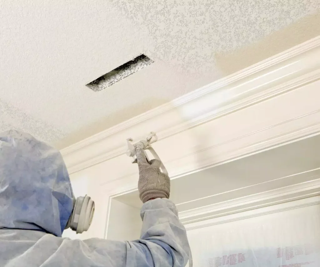 Professional texture repair technician spraying texture onto a ceiling. The newly applied texture seamlessly blends with the existing ceiling.