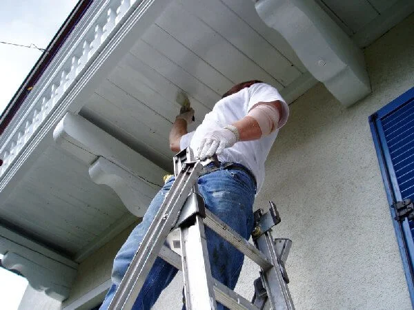 Professional painter high on a ladder painting exterior house trims white