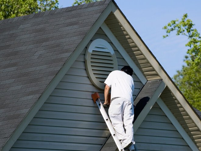 High on a lader , a painter  painting exterior house trims