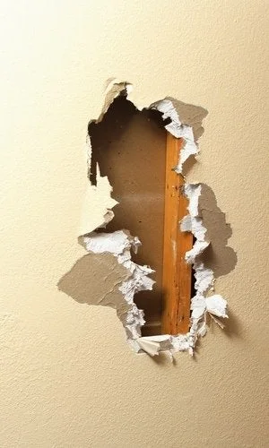 Large hole in a brown wall. Drywall severed and a wooden stud become exposed